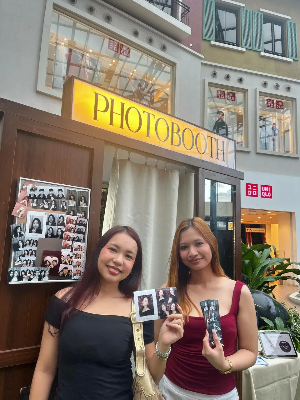 Two guests holding their keepsakes beneath the PHOTOBOOTH sign.