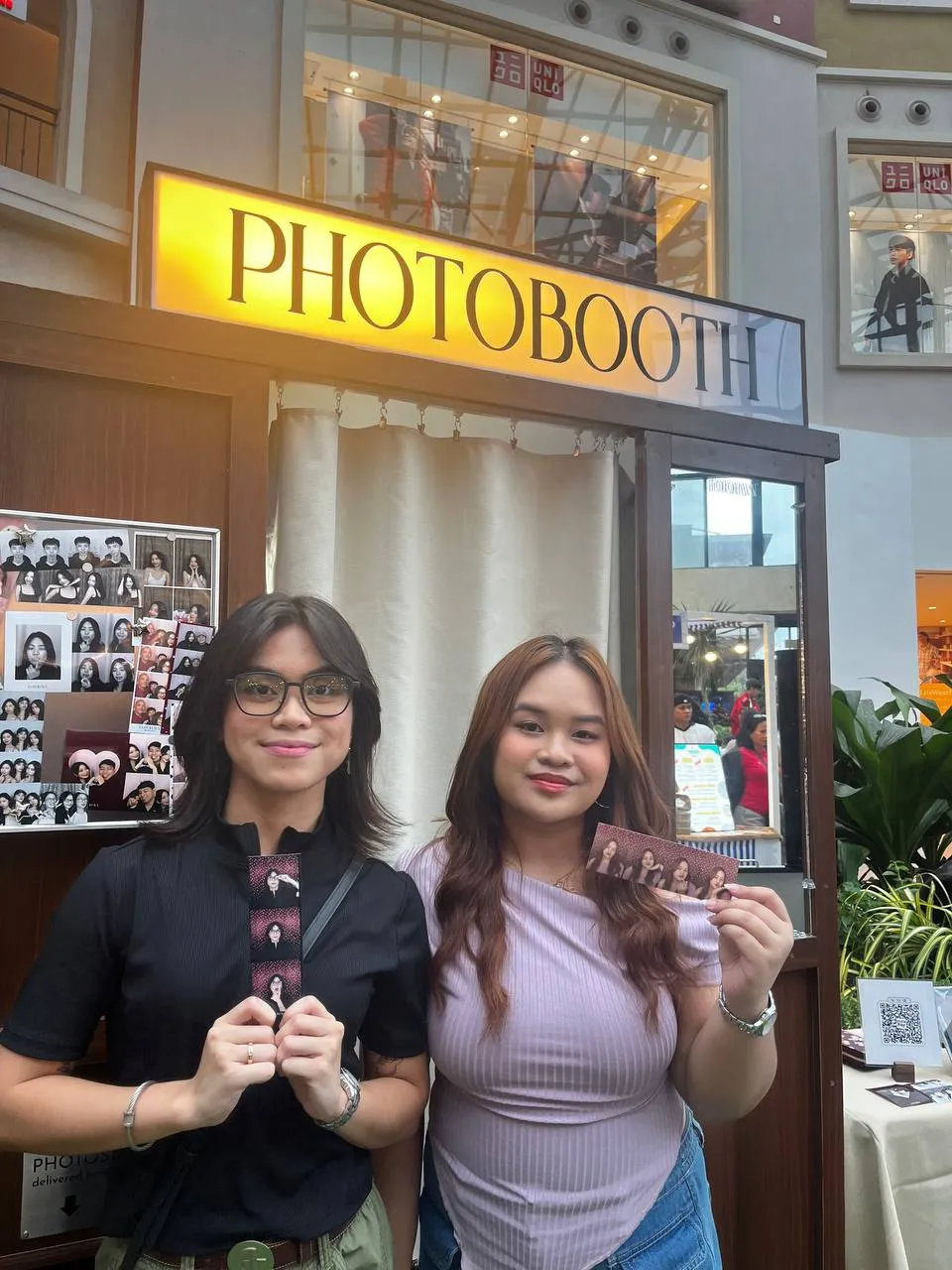 Two guests holding their prints beside the booth's grey photo display.