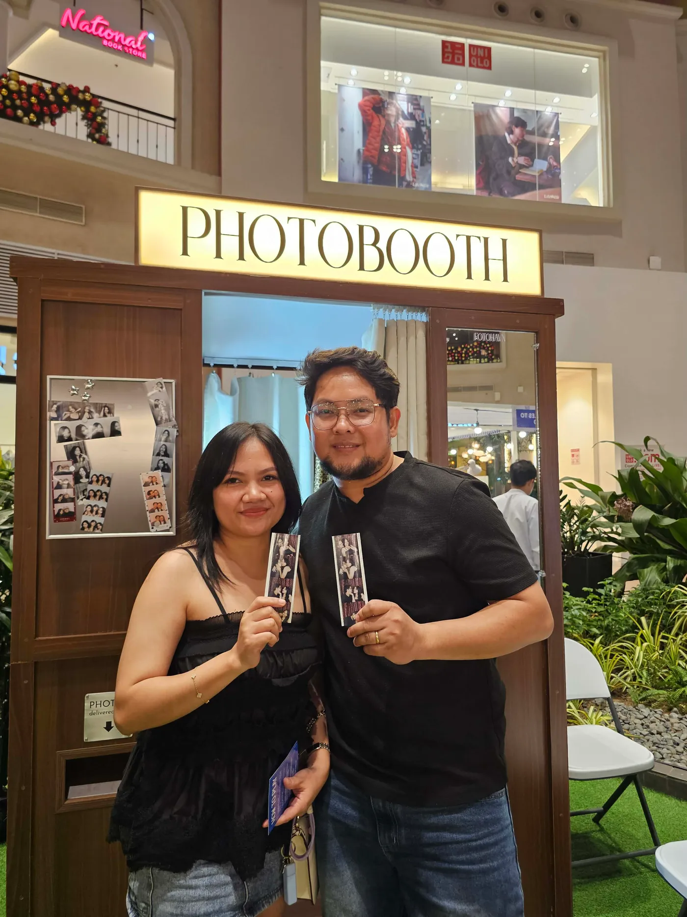 Two guests in dark clothing holding their Photo Strips beneath the booth sign.
