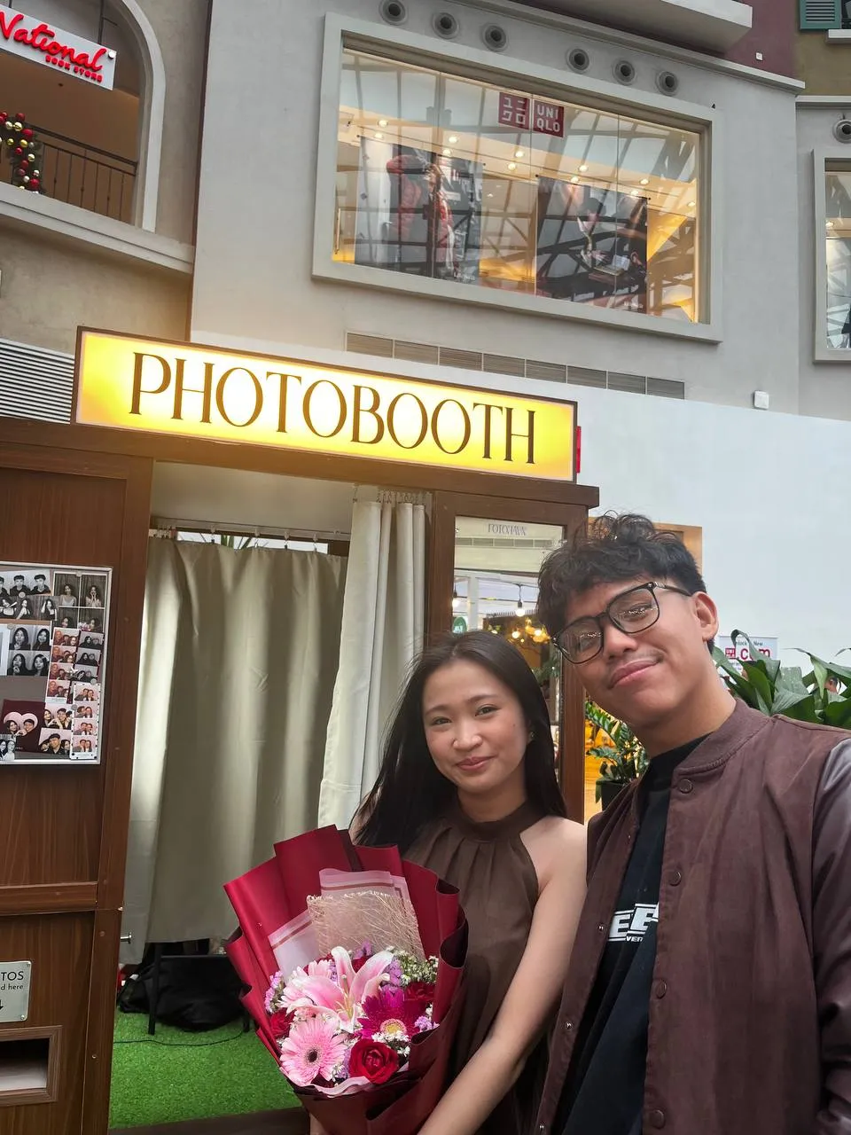 Two guests with a pink bouquet and printed photographs in front of the booth.