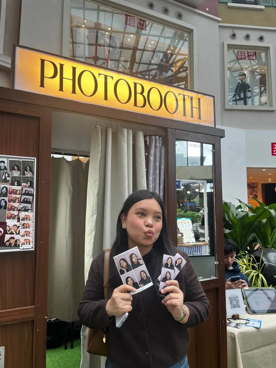 A guest in black holding two Photo Strips beneath the PHOTOBOOTH sign.