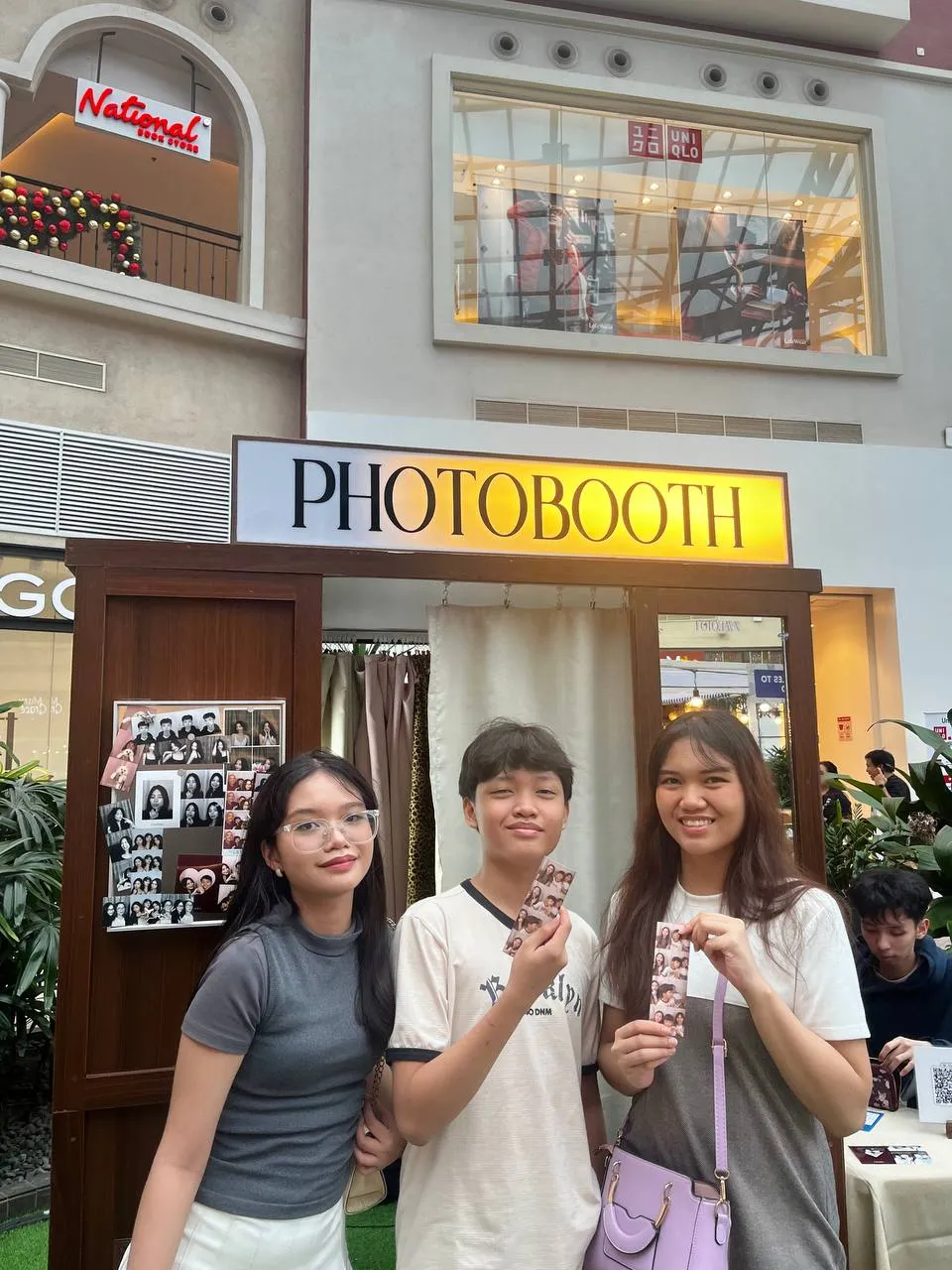 Three guests holding Photo Strips beside the booth's Jacobean Walnut exterior.