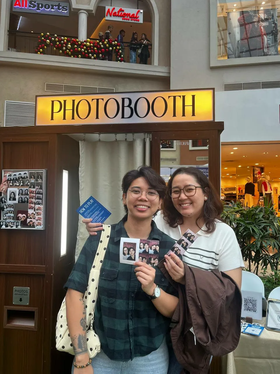 Two smiling guests holding photographs, one with a blue fan, at the booth.